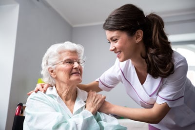 Pflegerin hilft Seniorin im Rollstuhl